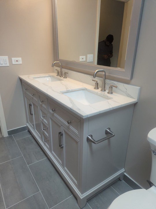 Bathroom vanity with marble top, framed mirror and tiled floor.