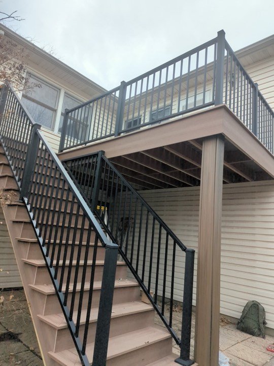 Deck staircase with black metal railing leading down from a raised deck.