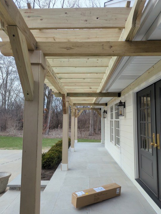 Heavy timber pergola over a covered patio with stone columns.