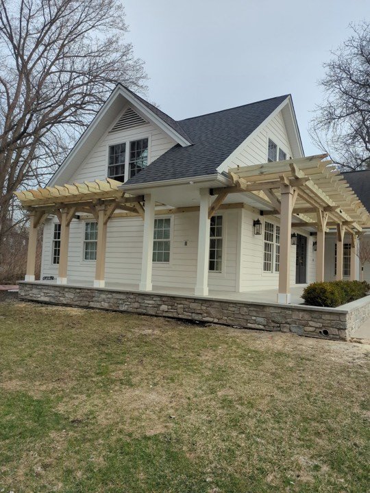 Pergola over the front porch of a white clapboard house.
