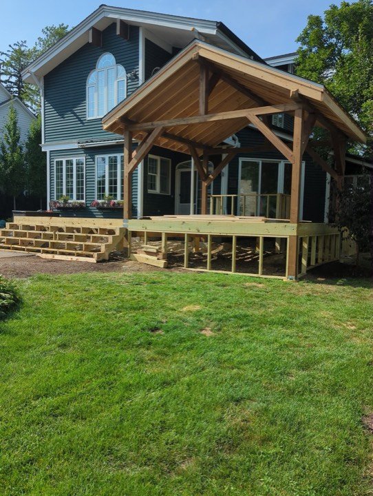 Cedar timber-frame covered porch with a gable roof on a dark blue-green house.